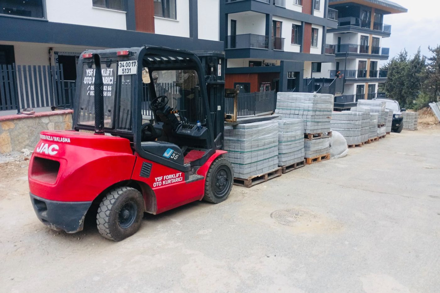 Şantiyede parke taşı paletlerinin yanında duran kırmızı JAC forklift