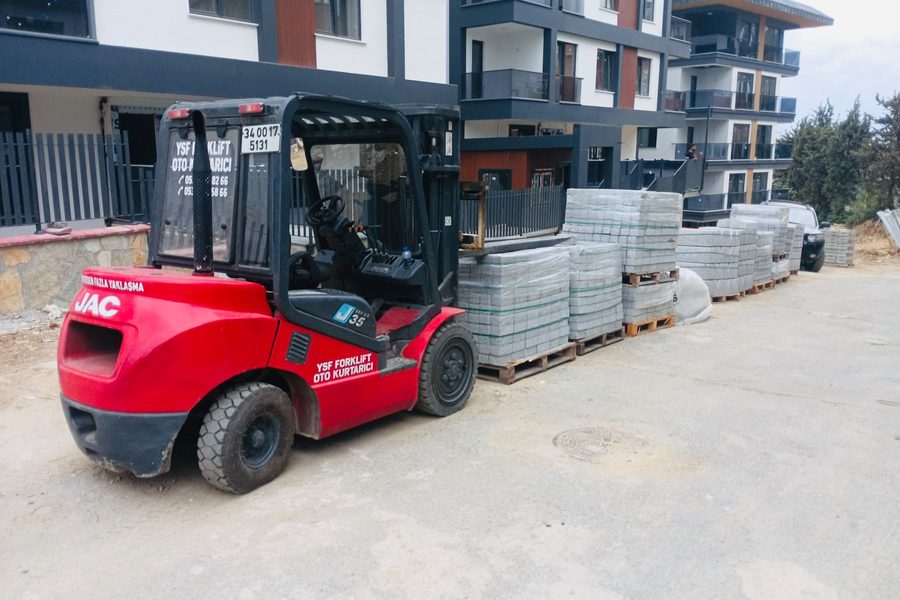 Şantiyede parke taşı paletlerinin yanında duran kırmızı JAC forklift