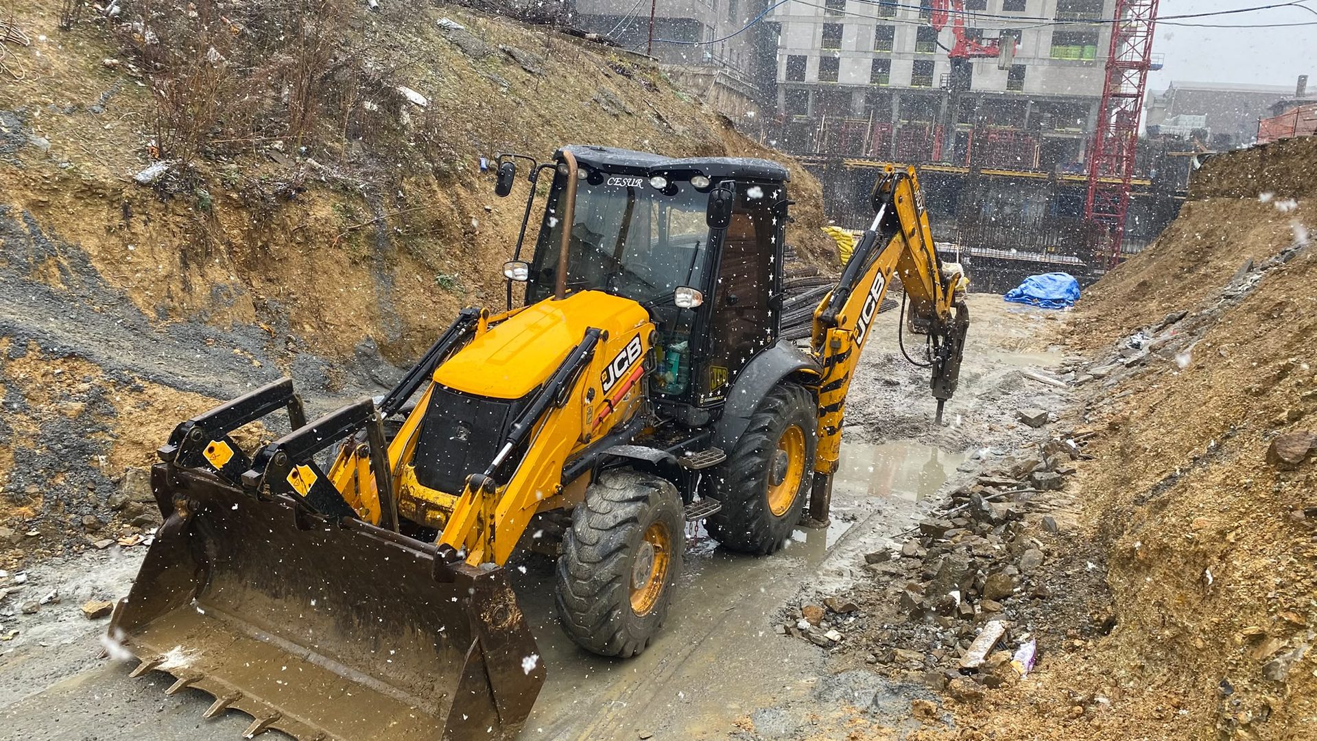 Kar altında temel kazısında kırıcı ataşmanla çalışan sarı JCB beko loder