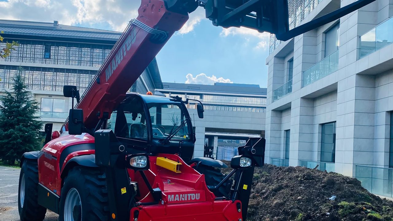 Kırmızı Manitou MT 1840 teleskopik yükleyici, çatalları bina hizasına kaldırılmış halde