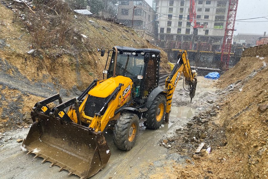 Kar yağarken temel kazısında kırıcı ataşmanla çalışan JCB kepçe