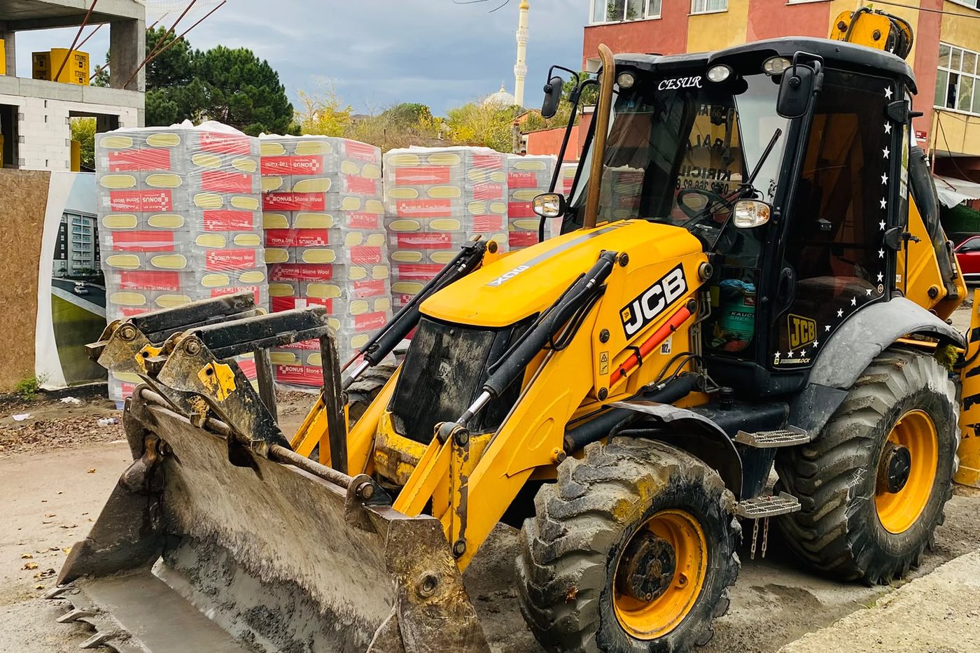 Şantiyede yalıtım malzemesi paletlerinin yanında bekleyen JCB kepçe