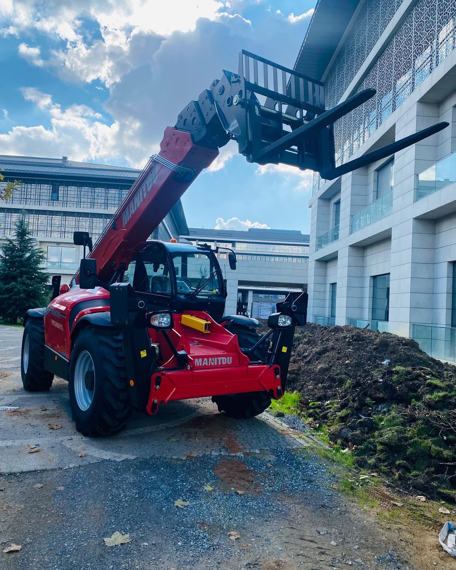 YSF Makina'nın kırmızı Manitou MT 1840 teleskopik yükleyicisi, çatalları bina hizasına kaldırılmış halde